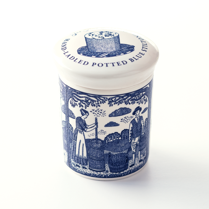 A blue and white jar decorated with rural scenes of cheese making with a lid that reads "Hand Ladled Potted Blue Stilton Cheese"