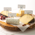 Reserve Cheese Collections on a wood slice tray. The Apline Swiss Cheese, the Parmigiano Reggiano, Herbed Soft, and Manchego cheese.