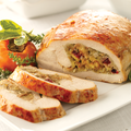 A sliced stuffed turkey breast on a white plate with garnish, showing a golden-brown crust and a stuffed filling.
